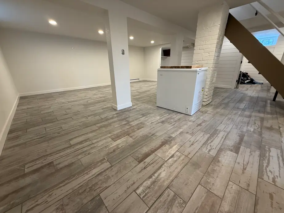A finished basement with a wood-look tile floor, recessed lights and white walls