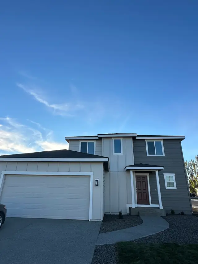 A small grey two-storey home with a white garage door under a wide blue sky