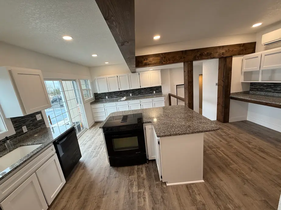 Renovated kitchen with white shaker cabinets, granite island and dark stained beams