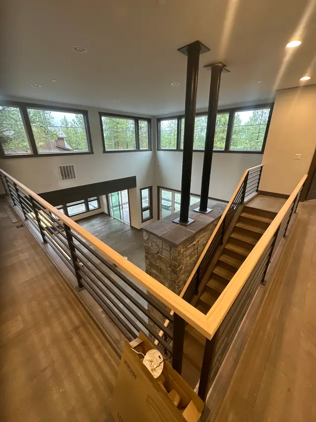 An open stair with a timber cap rail and black steel balusters beside a stone column, with clerestory windows looking into the pines